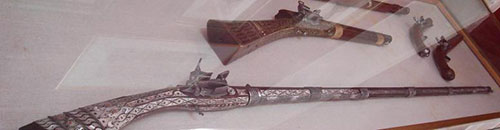 Μία «καραμπίνα» (άνω αριστερά), ζεύγος πιστόλων (δεξιά) και κάτω ένα μακρύκαννο καριοφίλι με περίτεχνη διακόσμηση (Αθήνα, Εθνικό Ιστορικό Μουσείο, φωτογραφ.: Περικλής Δεληγιάννης).